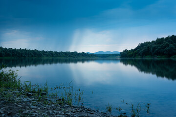 Landscape with river Sava and mountain in background during heavy rainfall, gloomy clouds reflecting in water surface