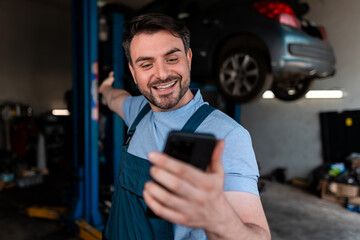 Mechanic enjoying a call in a busy garage while showing a car overhead