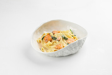 Tagliatelle pasta with salmon pieces and spinach in creamy sauce served in white bowl on white background