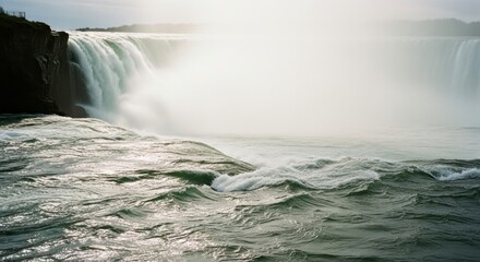 Powerful waterfall cascading over a rocky cliff. Turbulent river water with strong currents. Natural landmark with immense force and energy. Atmospheric misty landscape for travel and tourism