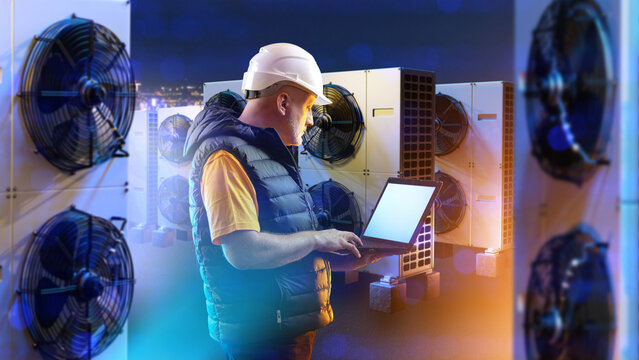 Man engineer servicing air conditioning equipment. Worker with laptop among ventilation units. Conditioning pumps supply building with clean air. Man adjusts ventilation equipment on computer.