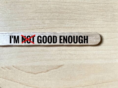 The phrase 'I'M NOT GOOD ENOUGH' written on a wooden stick, with the word 'NOT' crossed out in red marker.