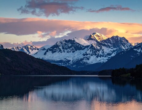 Majestic snow-capped mountain range reflected in a serene lake at sunset