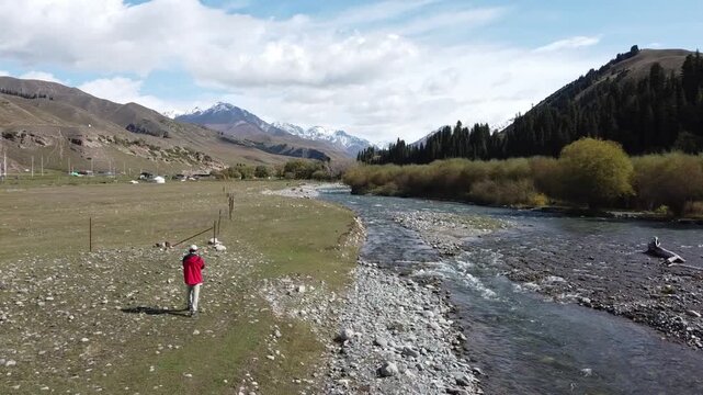 man flying drone over landscape of snow mountains and creek in xinjiang, china