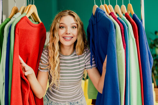Bright cheerful young woman shopping for colorful clothes in a fashion store with a big smile and vibrant wardrobe selection