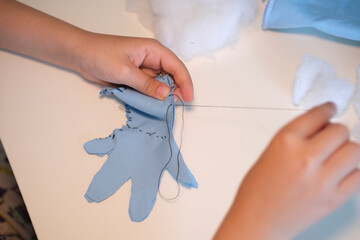 Top view. Children's hands hold a needle and thread and learn to sew.