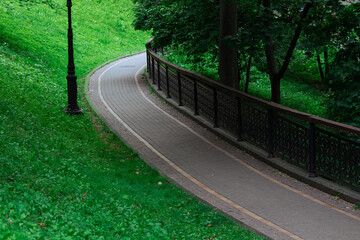 dusk park grass hill lawn landscaped by lantern and metallic fence with oval paved track for walking urban ordinary outside natural environment space