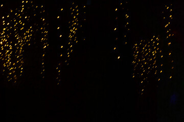 Golden light streaks hanging like a curtain over a pitch-black background, resembling a luminous rain or light shower.