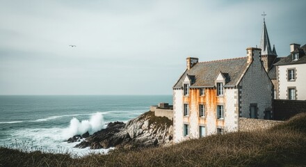 Historic stone manor on a dramatic seaside cliff. European coastal architecture with an ocean view. Waves crashing on a rocky shoreline. Travel destination and real estate concept