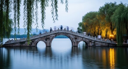 Ancient Chinese arch bridge over a tranquil lake at twilight. Long exposure with people in motion blur. Traditional Asian architecture and scenic landmark. Concept of time and journey
