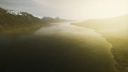 A serene river winds through a breathtaking mountain valley, bathed in the warm glow of sunset. Soft light illuminates the landscape, creating a peaceful atmosphere.