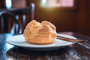 Choux pastry or cream puff freshly baked on a white ceramic plate on old wooden table in vintage style coffee cafe shop in a warm and comfortable atmosphere.