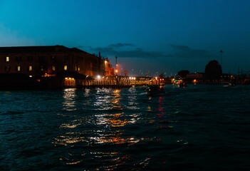 Venice, Italy - November 20, 2024: Nighttime view of a waterfront with illuminated buildings and boats reflecting on the water, creating a serene atmosphere in a coastal city