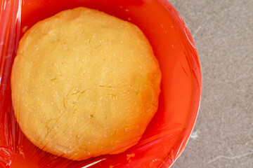 Raw dough in red bowl covered with plastic wrap, top view