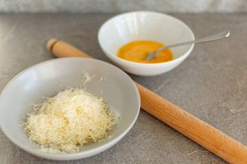 Gray bowl of grated cheese and yellow beaten egg with rolling pin, side view