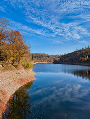 the Sengbach dam with reflections of the blue sky in the sunshine and the colorful autumn forest