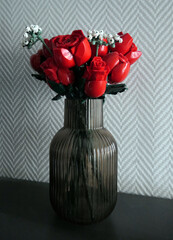A timeless bouquet: bright red roses from a construction set in a stylish ribbed vase. Creative interior decor against a backdrop of herringbone wallpaper. © Yullichik
