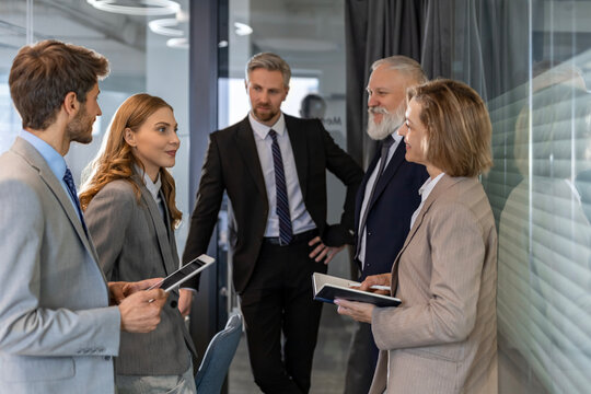 Group of business people standing together and discussing their work and projects, having a team meeting in an office.