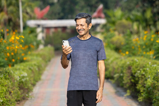 Indian Mature Man Walking and Checking Phone in Park, Active Technology Use