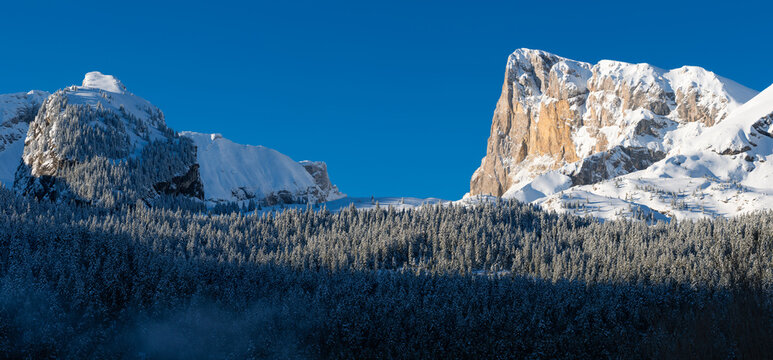 Aerial view of snow-covered limestone cliffs of Pic de Bure and Crete d’Ane in the Devoluy Massif, French Alps. Winter alpine panoramic landscape with forest and blue sky in the Hautes-Alpes, France