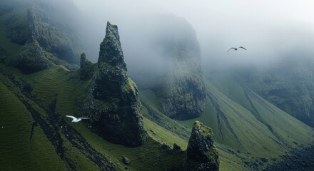Dramatic mountain landscape with jagged rock pinnacles. Misty morning fog over green mossy cliffs. Birds flying in a vast wilderness. Exploration and untamed nature concept for travel