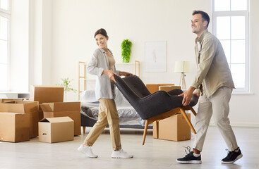 Moving couple in home with boxes, chair. They carry an armchair across a bright apartment,...