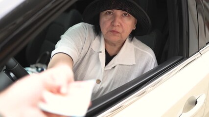 Mature woman inside a car gives euro banknotes to another person, looking into the camera, symbolizing payment, transaction, or financial exchange. 4K slow motion stock video.