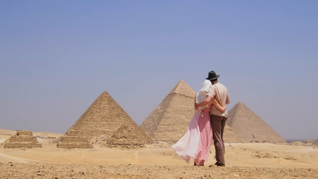 Couple embracing while admiring the pyramids in Egypt, enjoying a romantic moment during their desert vacation.
