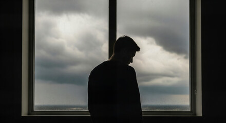 Pensive man standing alone gazing out window during stormy weather reflecting loneliness and introspection, emotional depth