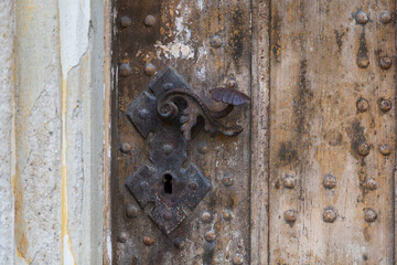 Antique and Rusted Ornate Door Handle with Escutcheon Plate and Keyhole on Old Wooden Church or Castle Door Panel