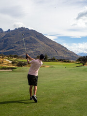 Obraz premium Golfer at Jack’s Point, Queenstown, New Zealand – Man in Pink Shirt Playing Golf with Scenic Mountain and Lake Wakatipu Views