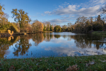 Fototapeta premium Late Autumn/Early Winter Scene by a Pond in a Historic Park: Reflections of Bare Trees and Willows in the Water on a Clear Day