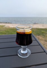 Close-up of a drinking glass on a table with a cola and lemon slices in the garden overlooking the sea.