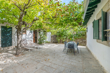 Extendable aluminum and tempered glass table on a patio surrounded by stone walls with natural shade from centuries-old magnolia trees