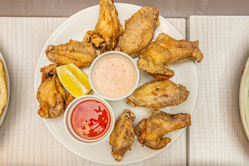 Tall stack of extra crispy chicken wings with varying levels of spice, served with three dipping sauces: BBQ, mango-habanero, and garlic-parmesan