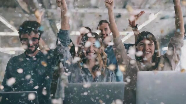 Happy coworkers cheer and throw confetti while working on laptops in a contemporary workspace. The image captures excitement, unity, and a dynamic atmosphere of success and innovation
