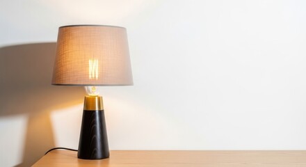 A table lamp with a beige lampshade and a black base, casting a warm glow on a wooden table.