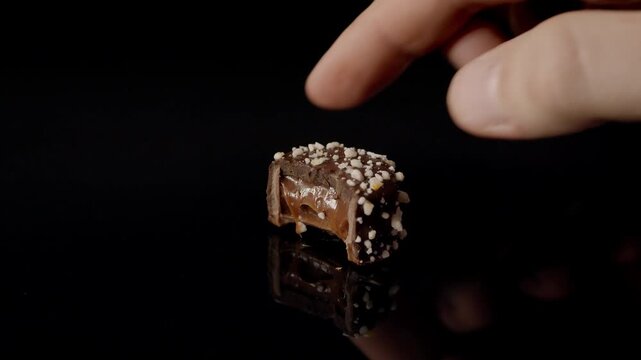 Chocolate praline coated with crushed nuts resting on glossy black reflective surface in closeup view