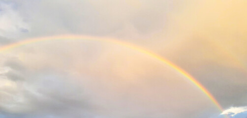 Rainbow across a warm sky over soft clouds, a serene moment of natural beauty