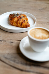 Elegant breakfast with coffee and croissant on light wooden table