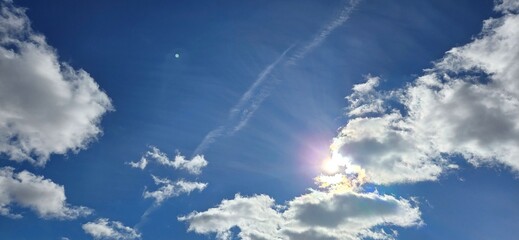 A vibrant blue sky scattered with white clouds, with the sun partially hidden creating beautiful...