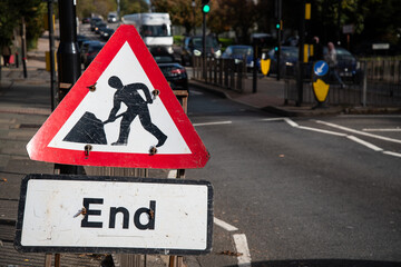 Triangle roadwork warning sign with “End” on a white sign, placed by the roadside in the UK,...