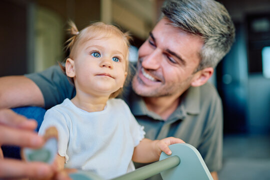 Happy father with gray hair looking at his curious toddler daughter with blue eyes and blonde pigtails in a domestic setting