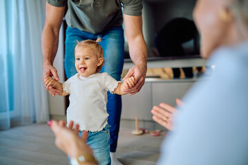 Happy baby learning to walk with parents' support, making significant first steps in a warm domestic environment