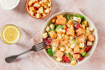 caesar salad with salmon, with croutons and dressing, in a salad bowl, on a pink table,