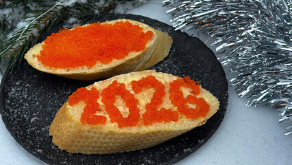 A sandwich 2026 with red caviar and a glass of champagne against the backdrop of a snowy Christmas tree.