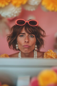 Fashionable woman with short hair and pink sunglasses looking over a computer screen. Retro inspired contemporary portrait with bold colors and y2k fashion aesthetics.