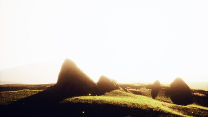 Rolling green hills rise against a bright sky as the sun begins to set. Long shadows stretch across the landscape, creating a peaceful and tranquil scene at dusk.