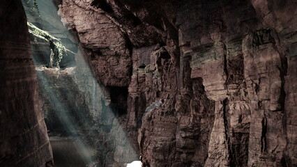 Sunlight streams through a narrow opening in a canyon, creating a magical atmosphere. The rocky walls show textures and shadows, inviting exploration and adventure.