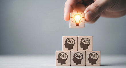 Hand placing a wooden block with lightbulb on top of head icons for creative thinking